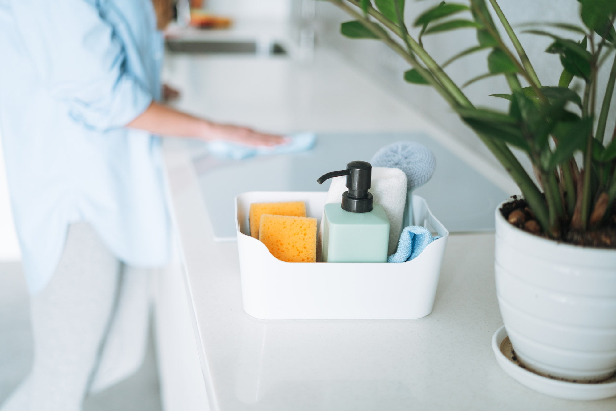 A woman is cleaning a kitchen counter with cleaning supplies.