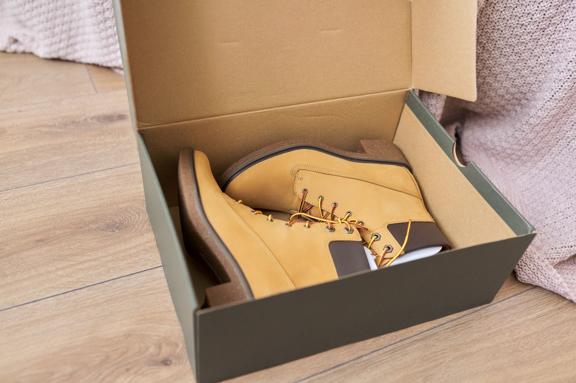 A pair of boots in a box on a wooden floor.