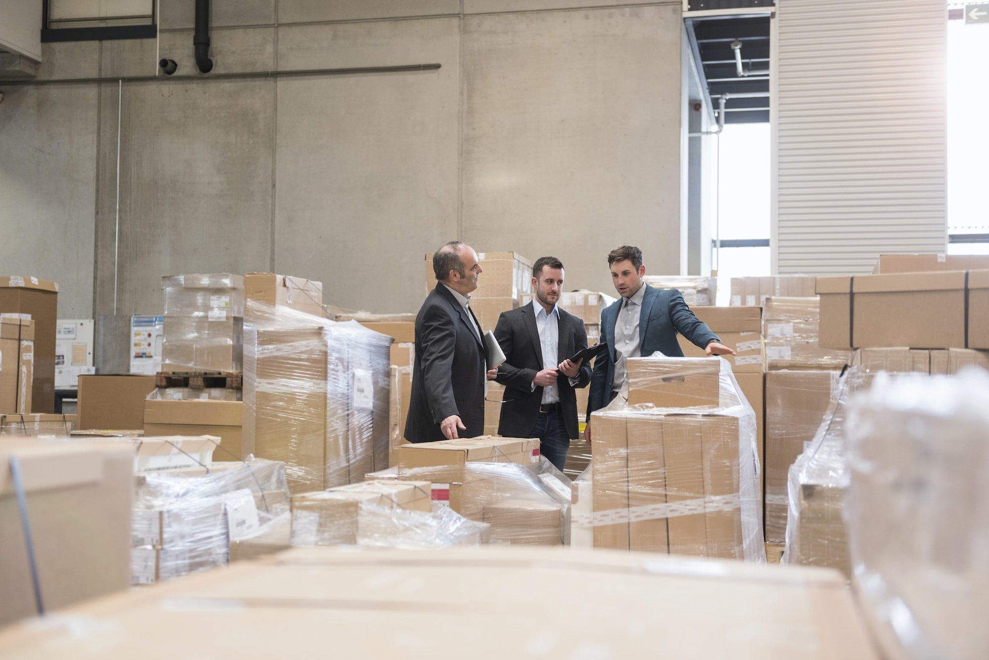 Three businessmen standing in a warehouse with boxes.