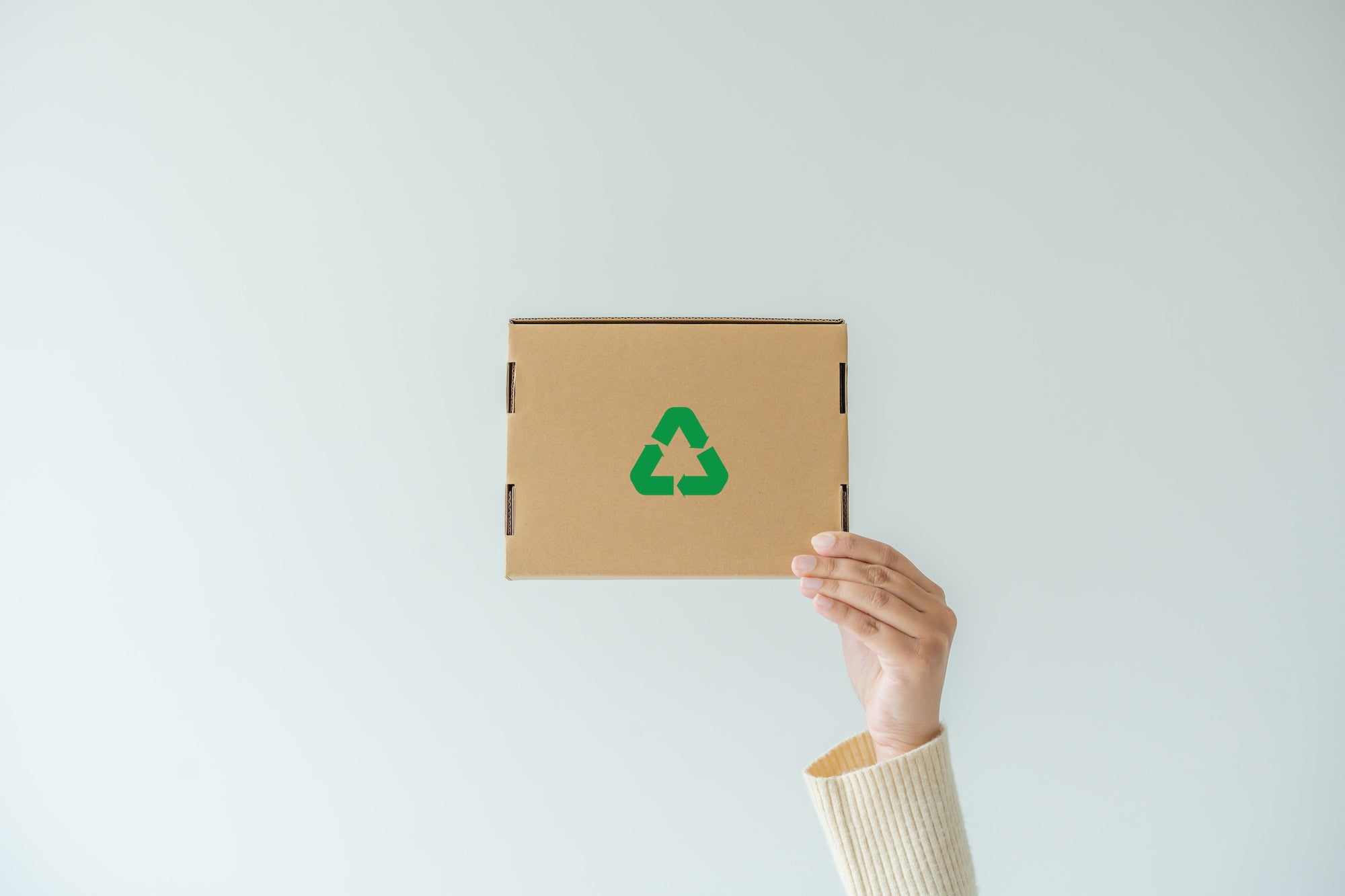 A woman holding up a cardboard box with a recycle symbol on it.