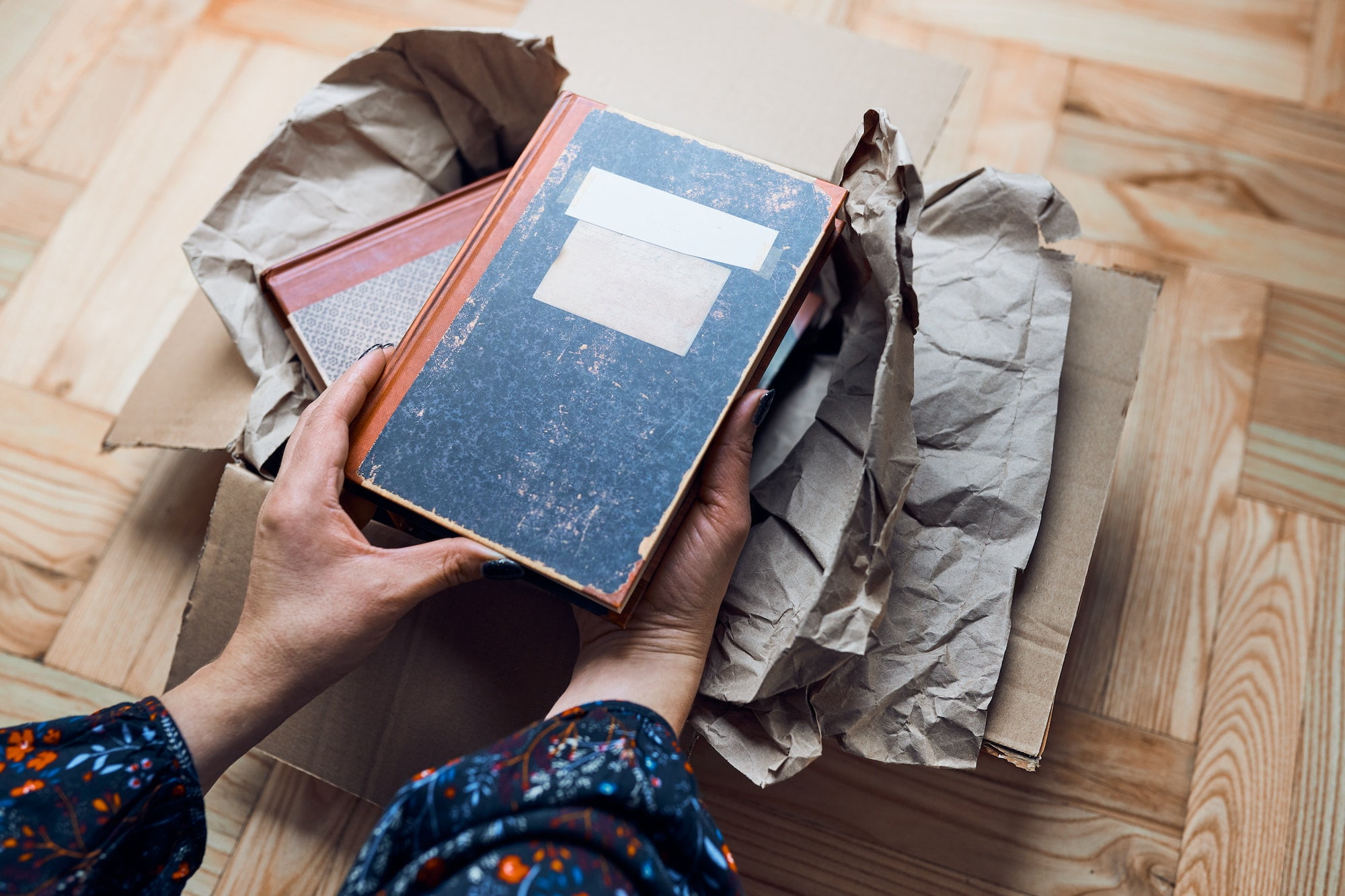 A person holding a book in a cardboard box.