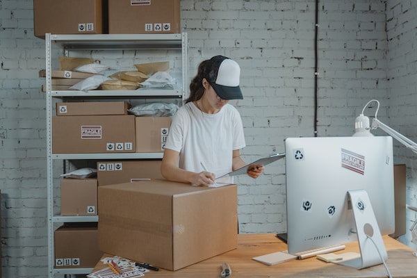 A woman packaging cardboard boxes at a desk in a warehouse.