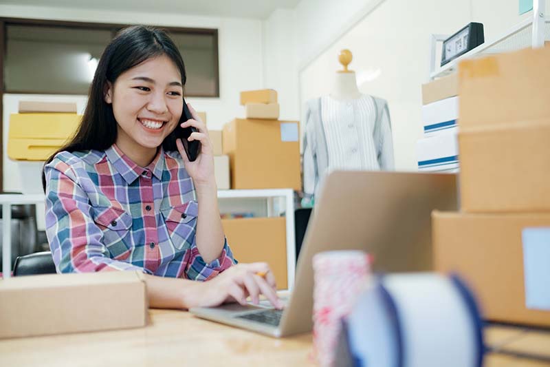 A woman is talking on the phone while sitting at a desk surrounded by custom-printed cardboard boxes.